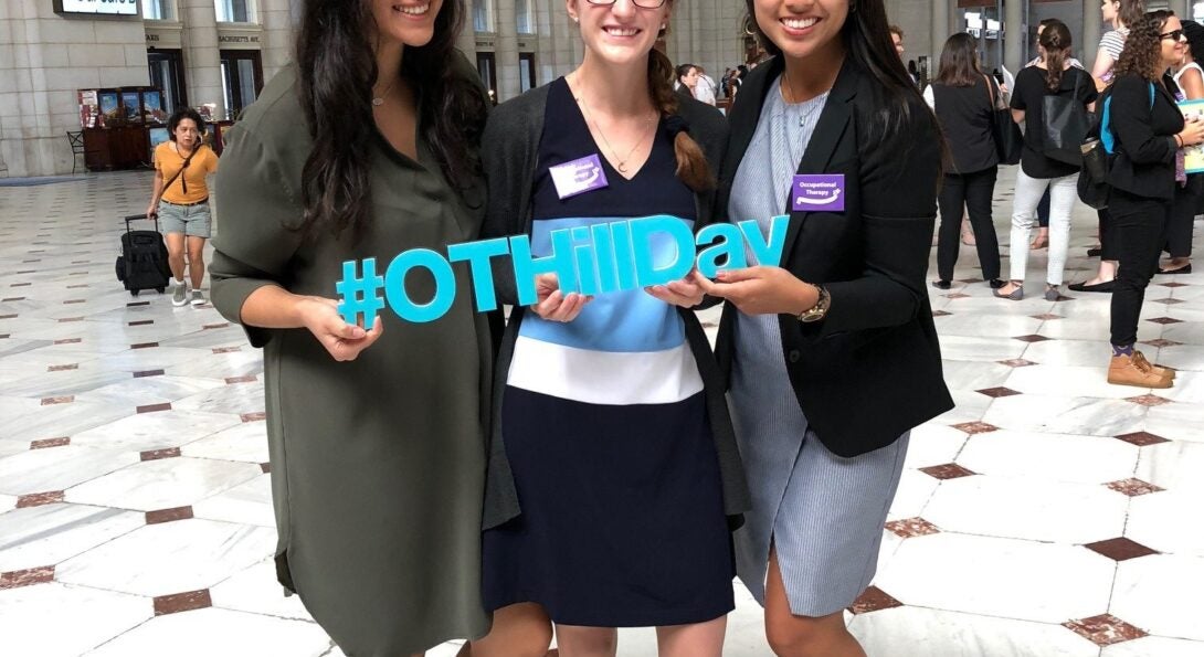 From left to right: Vivian Villegas, Victoria Turnbull and Megan Win on Capital Hill hold a sign that reads #AOTAHillDay