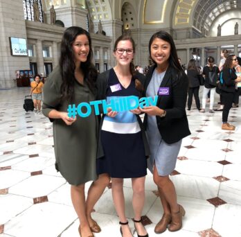 From left to right: Vivian Villegas, Victoria Turnbull and Megan Win on Capital Hill hold a sign that reads #AOTAHillDay
                  