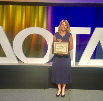 Liz Peterson stands holding her award certificate from AOTA
                  