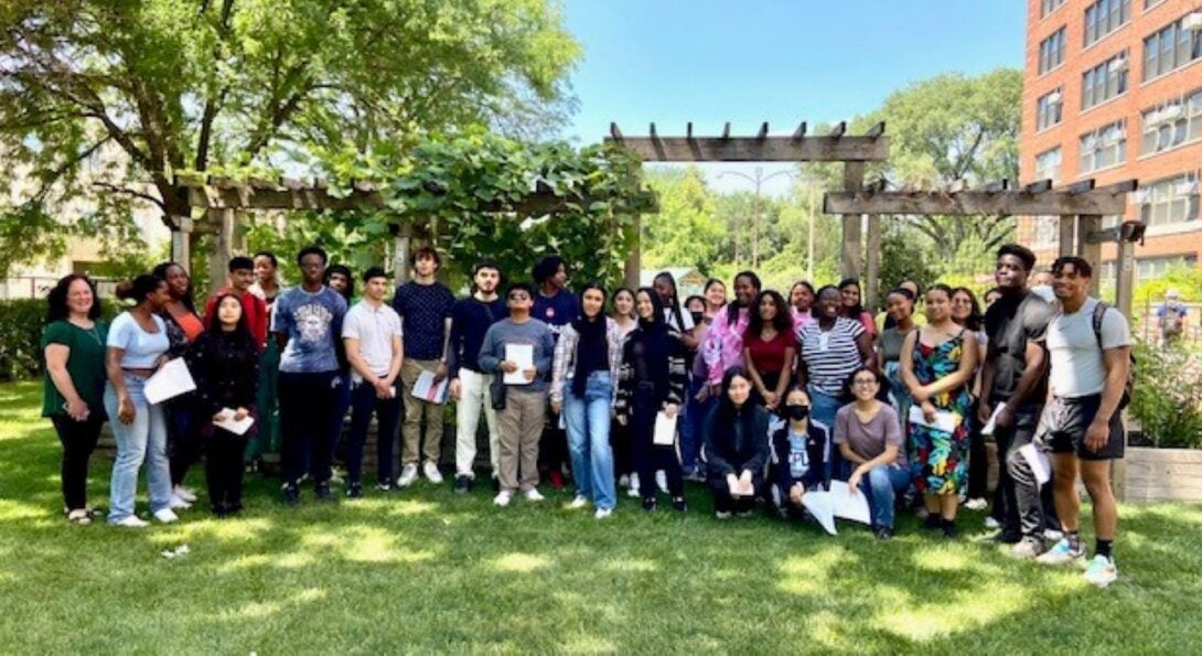 Group of students gathered on grass in front of AHS Nutrition Teaching Garden holding scavenger hunt flyers.