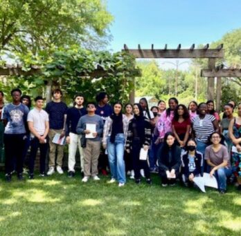 Group of students gathered on grass in front of AHS Nutrition Teaching Garden holding scavenger hunt flyers.
                  