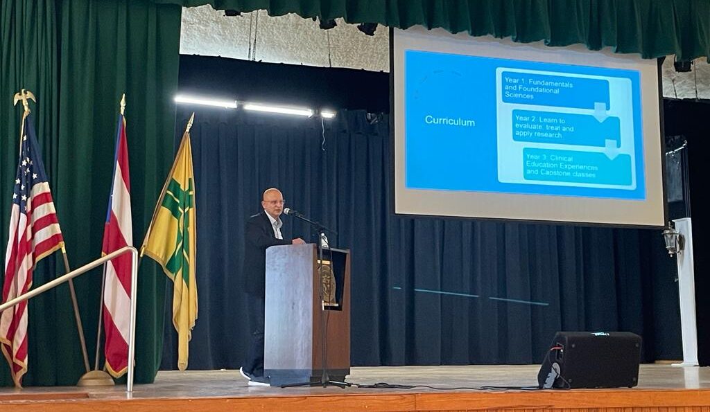 Carlos Crespo stand on a stage behing a podium while delivering a presentation