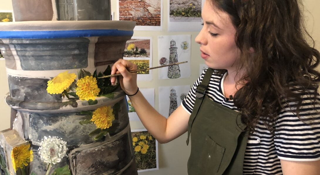 Kaitlin Stober paints yellow flowers on her lighthouse art installation piece