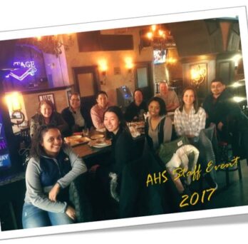 A group of AHS staff members sitting down around a rectangular dining table
                  