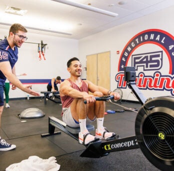 A F45 Coach motivates a student on the rowing maching
                  